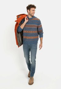 Blue knit sweater with patterned accents, orange puffer jacket draped over shoulder, denim jeans, and tan lace-up boots.