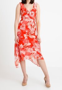 Abito floreale rosso con scollo a V e design a volant. Tessuto leggero e trasparente con fiori rosa. Orlo asimmetrico e maniche a tre quarti.