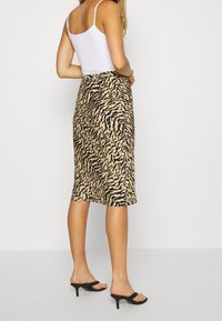 Djurtryck midi kjol i tan och svart, med en figurnära midja, mjuk textur och en lätt utsvängd nederkant. Matcher med svarta klacksandaler.