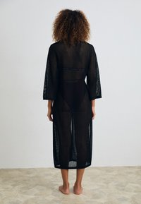 Mustad must läbipaistav kimono, millel on kolmeveerandi pikkuse varrukad, põlve alla ulatuv pikkus, avatud selg ja pitsdetailid vöökohtadel, kantuna paljajalu.