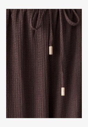 Brūna teksturēta auduma bikses ar elastīgu jostu un saites auklu, kuras izceļ zelta akcenti uz saites galiem.