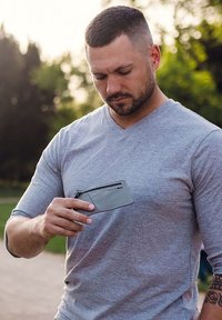 Gray zippered wallet held in a hand, made of smooth material. Features a logo on the front and a simple, rectangular design.
