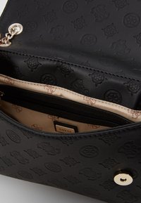 Zwarte tas van imitatieleer met een gegraveerd patroon, een beige binnenkant en een ritssluiting. Afgewerkt met een gouden drukknopsluiting en metalen details.