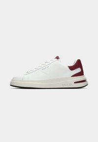 Hvit sneakers med en glatt lær-øvre, bordeaux suède-detaljer, flate lisser og en teksturert gummisåle. Har et logo på siden.