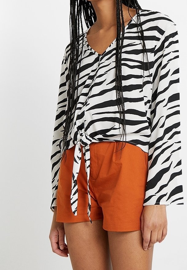 Femme portant un chemisier à manches longues rayé zèbre noir et blanc noué à la taille avec un short taille haute orange.