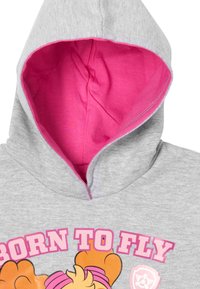 Felpa grigia con rivestimento rosa nel cappuccio. Presenta una stampa grafica con la scritta "BORN TO FLY" accompagnata da un personaggio dei cartoni animati e dettagli con emblema.