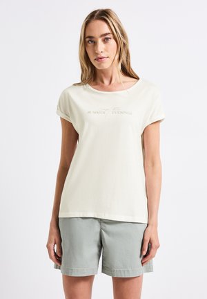 T-shirt beige clair à manches courtes avec un col rond et des poignets retroussés, arborant un imprimé minimaliste indiquant "SOIRÉES D'ÉTÉ".