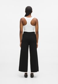 Fekete, bő szárú nadrág magas derékkal, bordázott textúrával és kontrasztos fehér szegéllyel, amihez egy szűk fehér ujjatlan felsőt viselnek.