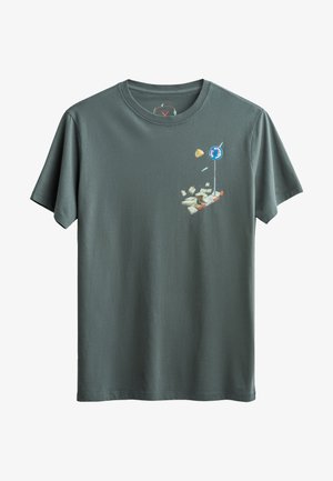 T-shirt en coton vert foncé à manches courtes. Présente un design graphique coloré d'objets flottants, y compris un panneau de circulation et des papiers.