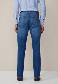 Jeans de denim azul oscuro con corte recto, que cuentan con dos bolsillos traseros y un parche de cuero marrón en la cintura.