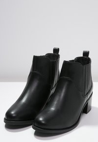 Czarne skórzane botki za kostkę z okrągłym noskiem, elastycznymi bocznymi panelami i słupkowym obcasem. Gładka tekstura z minimalnymi detalami przeszycia.