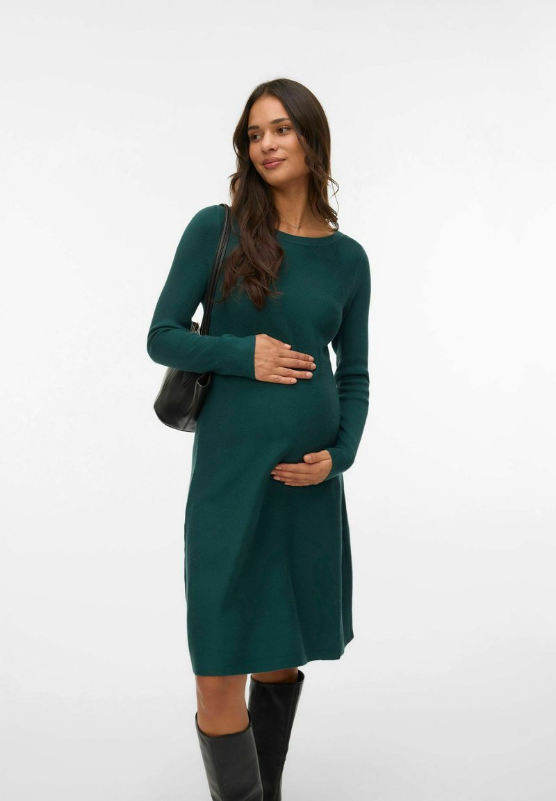 Knälång, figurformad grön stickad klänning med långa ärmar och rund halsringning, i kombination med knähöga svarta stövlar och en liten svart väska.