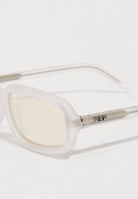 Läpinäkyvät valkoiset aurinkolasit, joissa on neliönmuotoiset linssit ja hopeiset yksityiskohdat. Sisältää RSF-brändäyksen sankassa ja teksturoidut varret.