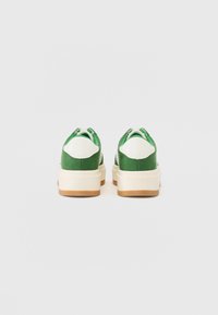 Tenisi verzi din suede cu accente albe, având o talpă groasă albă și o talpă exterioară din cauciuc gumos. Designul include un guler și o limbă căptușite.