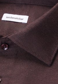 Camicia marrone con bottoni, realizzata in un tessuto con trama testurizzata, con etichetta Seidensticker vicino al colletto e un bottone scuro vicino alla scollatura.