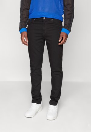 Jeans en denim noir avec une coupe slim, un design à cinq poches, des boutons en métal argenté et des accents bleus contrastants sur une chemise à manches longues en maille noire.