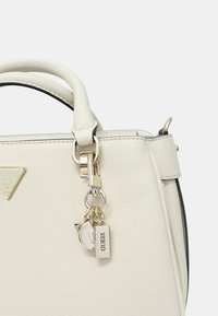 Borsa a tracolla in pelle sintetica bianca con due manici superiori, accessoriata con hardware argentato e un charm con un'etichetta e un design di gatto.