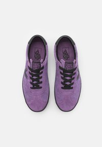 Sapatilhas de camurça roxas com atacadores e detalhes pretos. Apresentam um bico arredondado e sola de borracha preta contrastante. Etiquetas visíveis no interior.