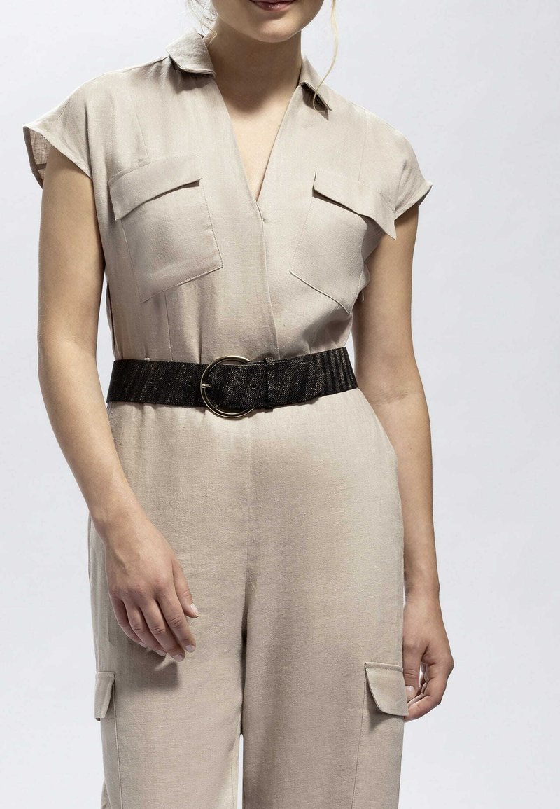 Beige jumpsuit med korta ärmar, två fickor med lappar, en V-ringning och ett strukturerat svart bälte med en cirkulär spänne.