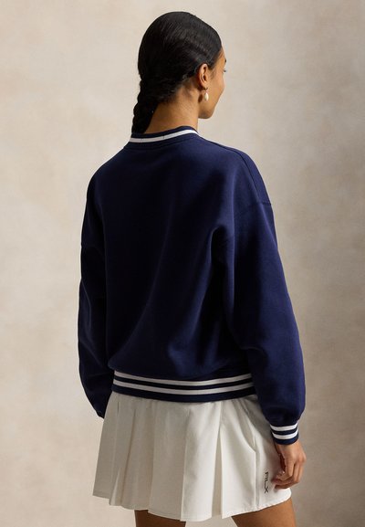 Μπλε ναυτικό φούτερ με λευκές ribbed μανσέτες και τελείωμα, με λαιμόκοψη crew και χαλαρούς ώμους, σε συνδυασμό με λευκή πλισέ φούστα.