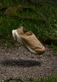 Pantofii slip-on bej, cu o textură căptușită, design ușor și talpă din cauciuc. Prezintă o bandă de prindere în spate și accente subtile cu dungi.