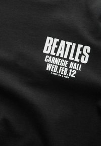 Schwarzes Baumwoll-T-Shirt mit fettem weißen Text, der "BEATLES CARNEGIE HALL MITT. 12. FEB." lautet, mit zusätzlichen Details darunter.