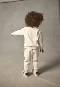 Helebeežidest spordiriietus, mis koosneb pika varrukaga topist ja kitsenevatest pükstest. Pehme tekstuur, voolujooneline disain, õrnad soonikkoes mansetid ja ümara kaelusega.