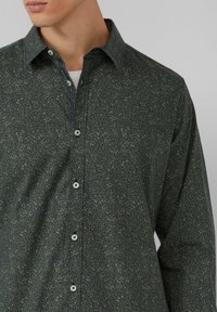 Chemise à boutons vert foncé à motif floral, dotée d'un col classique, de manches longues et de boutons de couleur claire.