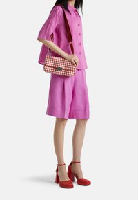 Růžový dvoudílný lněný outfit s krátkými rukávy a kraťasy, doplněný červenou károvanou kabelkou a červenými botami na platformě.