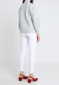 Jersey gris de punto con cuello alto, combinado con jeans ajustados blancos y tacones de gamuza rojos tipo slingback con tacones en bloque y correas en el tobillo.