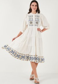 White midi dress with tiered design, puff sleeves, and blue and yellow floral embroidery along the hem and bodice. Soft textured fabric.