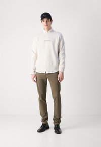 Lys grå hettegenser med "Calvin Klein Jeans" logo, over en hvit skjorte med krage; olivengrønne bukser; svarte sko; svart caps. Minimalistisk design.