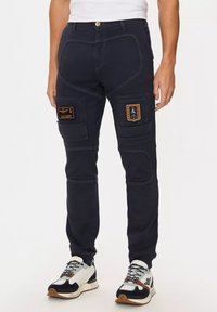 Pantaloni cargo blu navy con cuciture a contrasto, numerose tasche cargo e toppe ricamate. Presentano una vestibilità slim e un tessuto elasticizzato.