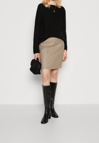 Zwarte gebreide trui, beige aansluitende rok en kniehoge zwarte leren laarzen. Houdt een gestructureerde zwarte handtas vast. Eenvoudig, modern ontwerp.