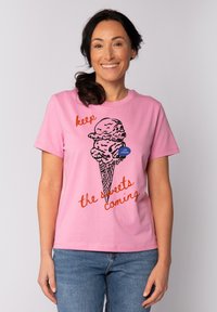 Pinker Baumwoll-T-Shirt mit einem Grafikdesign eines Eisbechers in schwarzer Umrandung und rot-orangem Text "Halt die Süßigkeiten nach." Kurze Ärmel, Rundhalsausschnitt.