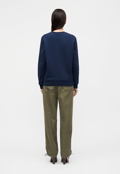 Μπλε σκούρο φούτερ με στρογγυλή λαιμόκοψη, ριμπ μανσέτες και ραφή πίσω, σε συνδυασμό με χακί παντελόνια με κορδόνια στα τελειώματα.