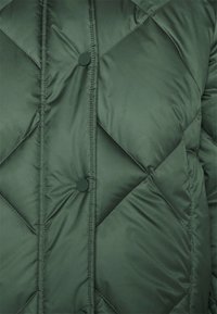 Grøn polstret jakke med en diamantquiltet mønster, der har runde knapper og en glat, blank overflade.