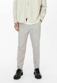 Pantaloni a righe di colore chiaro con una vestibilità affusolata, realizzati in tessuto morbido. Abbinate a scarpe nere testurizzate e a una camicia beige.