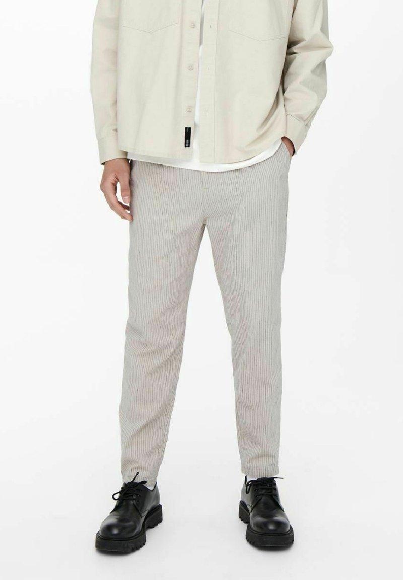 Pantaloni a righe di colore chiaro con una vestibilità affusolata, realizzati in tessuto morbido. Abbinate a scarpe nere testurizzate e a una camicia beige.