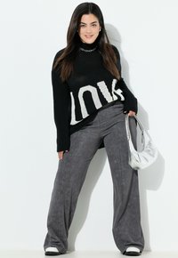 Sort strikket sweater med hvid "LOVE" tekst, parret med grå brede bukser. Tilbehør med en sølv håndtaske og hvide sneakers.
