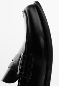 Sort lædersko med rundet tå, der har en dekorativ rem og syningsdetaljer langs kanten. Glat tekstur, elegant design.