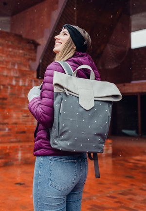 Gray backpack with white polka dots and a gray flap, made of durable material. Features two shoulder straps and top handle.