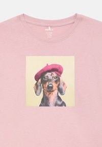 Maglietta rosa chiaro con colletto rotondo che presenta un'immagine stampata di un bassotto che indossa un berretto bordeaux su uno sfondo giallo pallido.