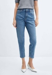 Jeans de mezclilla de color azul claro con una cintura alta, corte ajustado y longitud hasta el tobillo. Combinados con una blusa gris ajustada y tacones blancos de punta. 