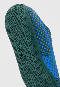 Baskets bleues avec semelles noires comportant un motif texturé d’usure de pneu et un petit logo Puma sur la semelle.