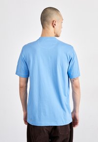 Camiseta de algodón azul claro con escote redondo y mangas cortas. La parte trasera presenta una textura suave y un diseño sencillo sin adornos.