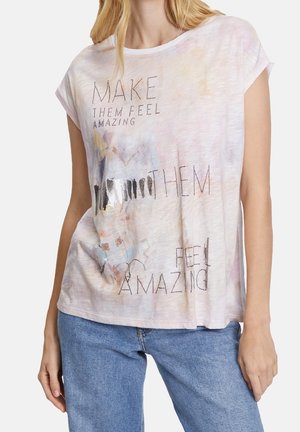 Vrouw draagt een lichtroze shirt met korte mouwen met de tekst "MAKE THEM FEEL AMAZING" en abstracte patronen in aquarelstijl.