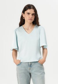 Top azzurro chiaro a maniche corte con scollo a V, realizzato in tessuto morbido. Presenta maniche leggermente arricciate, indossato con jeans chiari.