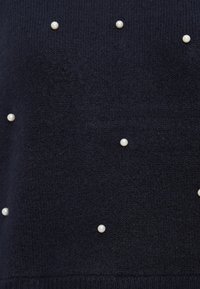 Marineblauwe gebreide trui met een gestructureerd oppervlak en verspreide witte parelaccenten voor extra detail.