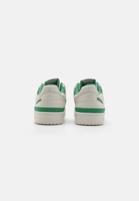 Sneakers with a smooth, off-white leather upper, green accents on the heel and midsole, featuring a textured rubber outsole and padded collar.